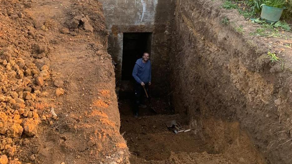 A man in a blue jumper smiles as he works near the entrance of a German bunker found under a Guernsey house.