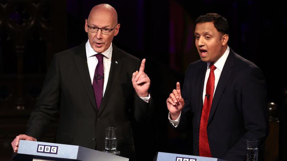 John Swinney and Anas Sarwar at a BBC election debate, both with mouths open in mid sentence and their fingers held aloft