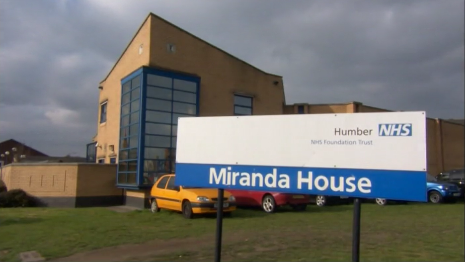 The outside of Miranda House, Hull. The yellow brick building has blue window frames and stands behind a blue and white NHS sign.
