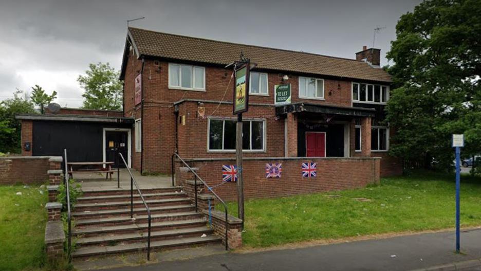 Steps from a pavement lead up to  pub, Union flags have been fixed to a wall