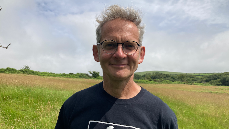 Adam Dawson who has grey hair and glasses, standing in a grassy field