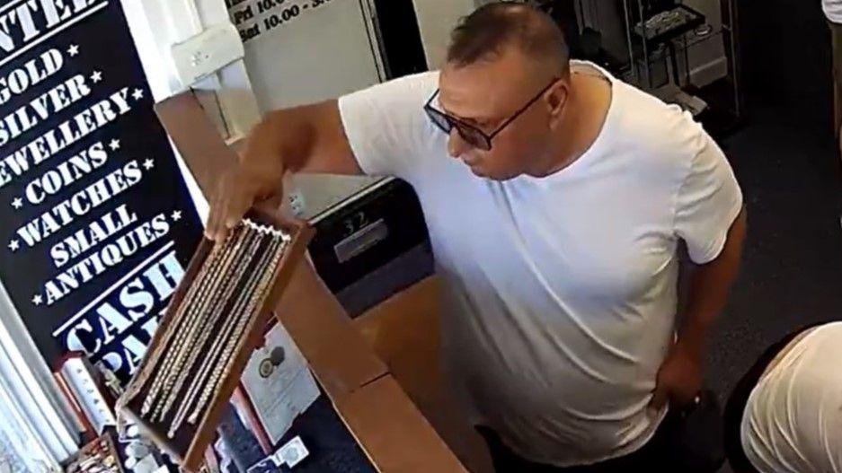 Vadar-ghimes Agafitei wearing a white t-shirt and sunglasses leaning over a counter and taking a wooden board with a number of gold chains on it