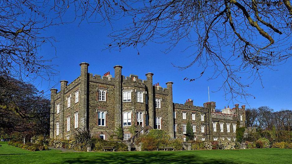 The exterior of the nunnery a grand brown three-storey building with a large field in front on a clear blue day.