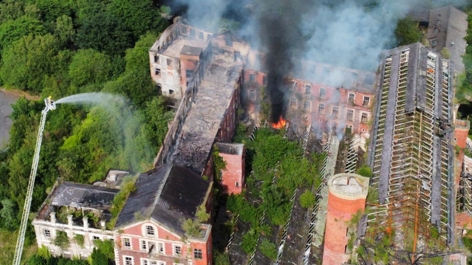 Another aerial photo of the fire at HIlden Mill in June 2021.  The picture shows smoke rising from derelict Victorian buildings and firefighters using an aerial hose to dampen the flames. 