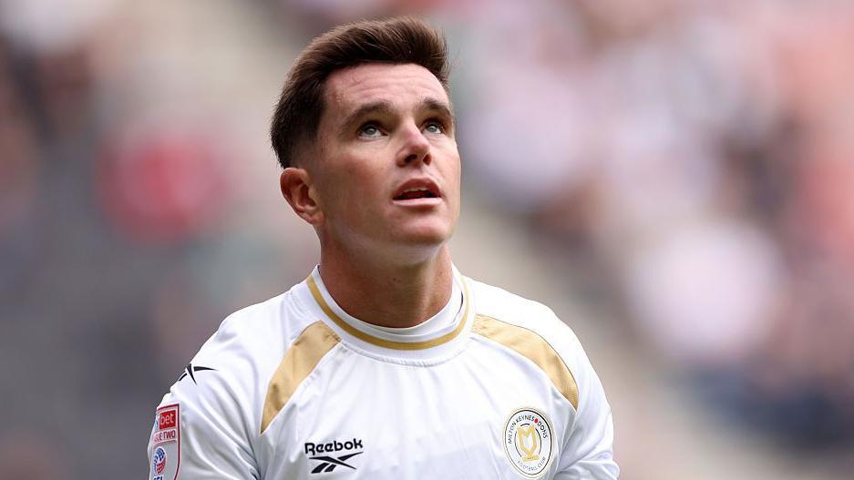 Liam Kelly in a white and gold MK Dons jersey during a match.