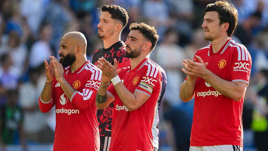 Manchester United players in red shirt, including Bruno Fernandes (centre) and Harry Maguire (right), applaud the crowd.