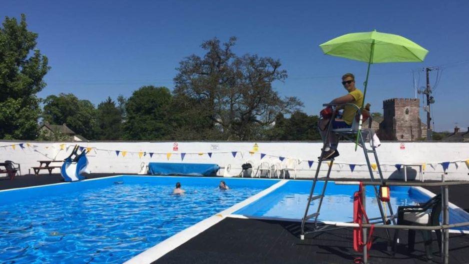 A lifeguard on a high chair with a sunshade, watching over two swimmers