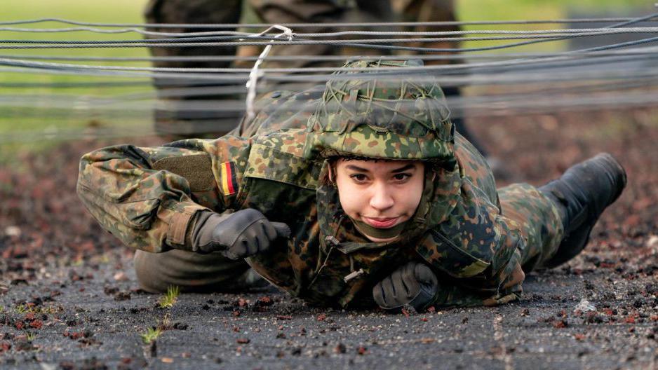 A soldier crawls under wires during German military training, 2021