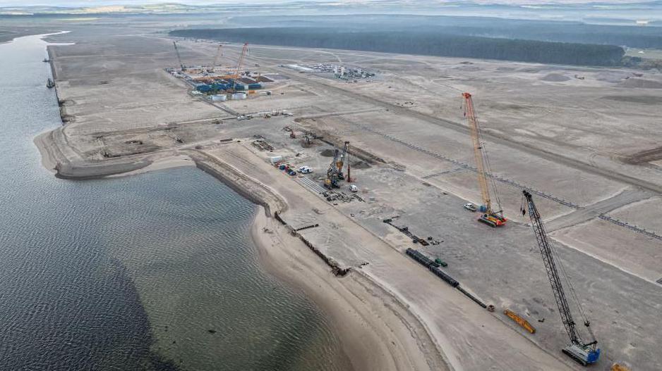 An aerial view of the yard at Ardersier. It is an expanse of sandy ground by the sea. A number of large cranes are on the site.