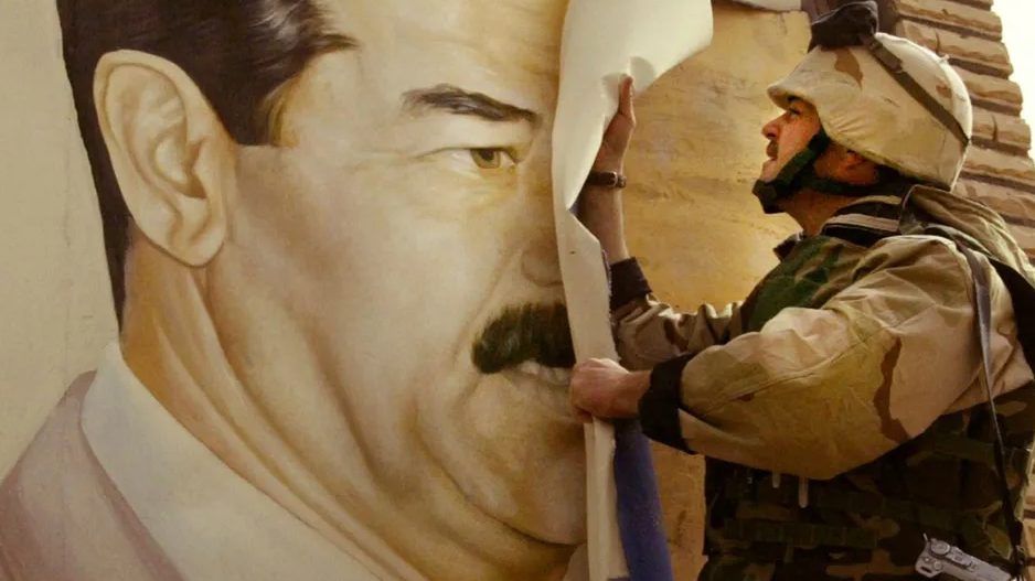 A soldier covers up a mural of former Iraq dictator Saddam Hussein