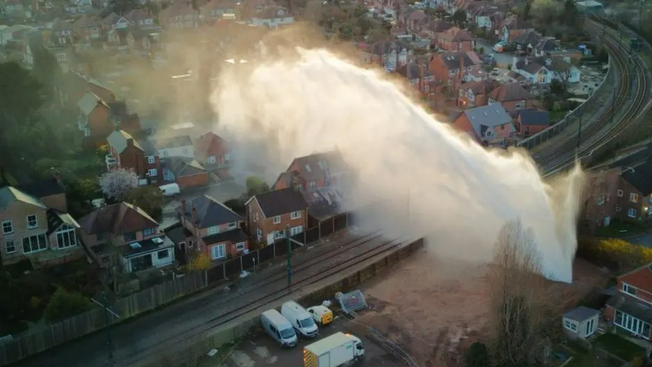 An aerial image of a ruptured water main with a large water spray covering tram tracks and a number of homes