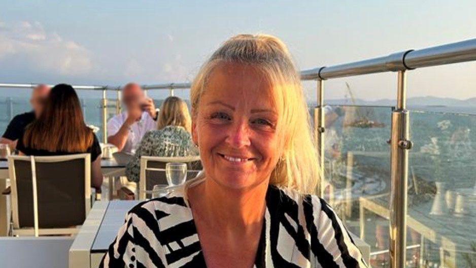 Anita Rose is pictured in a roof top dining establishment, smiling with her blonde hair tied back. She is wearing a black and white top.