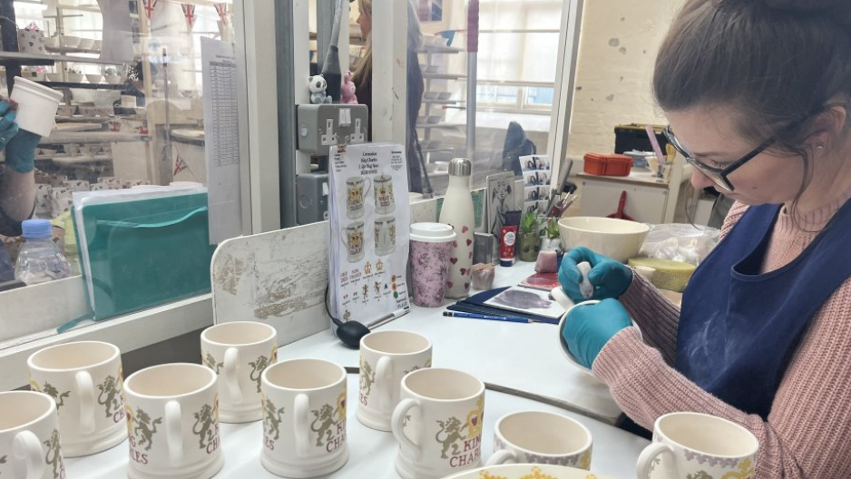 A woman applies decorations to white ceramic mugs