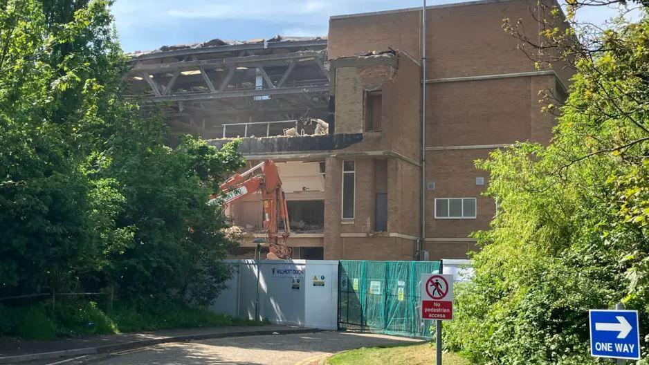Demolition of the pool building, with a demolished frontage and an orange digger in front of it.