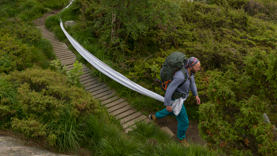 A man with a backpack walking on a path surrounded by forest