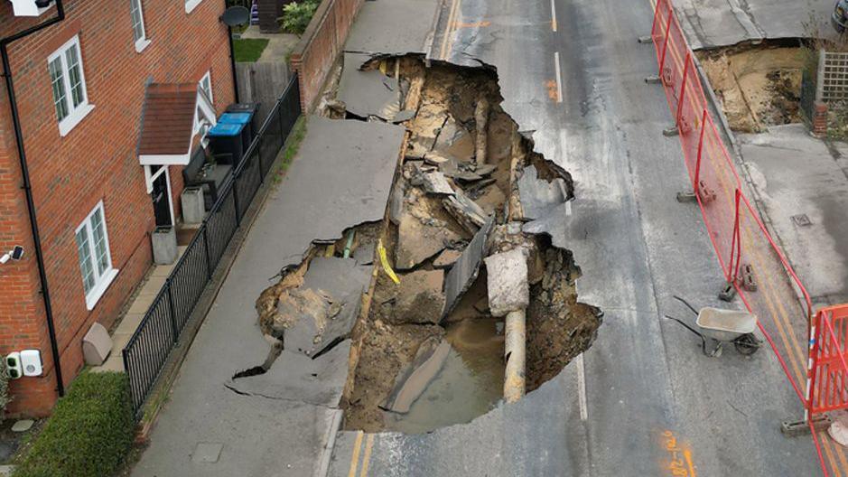 An aerial view of Godstone High Street showing the sinkholes. The street is cordoned off and houses line either side of the street.