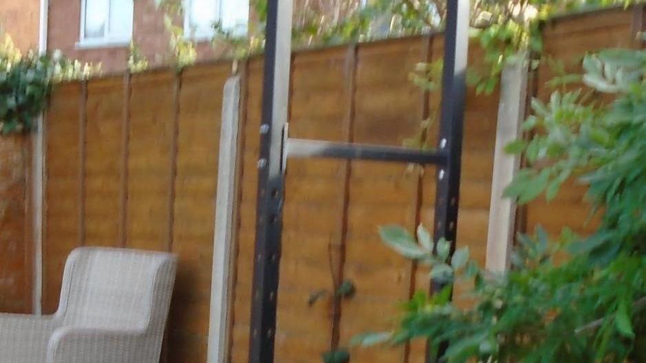 A slightly blurry image of an exercise pull-up bar in a garden with a fence behind