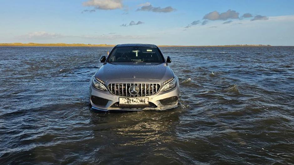 A Mercedes silver car in the North Sea. The wheels are submerged by water.