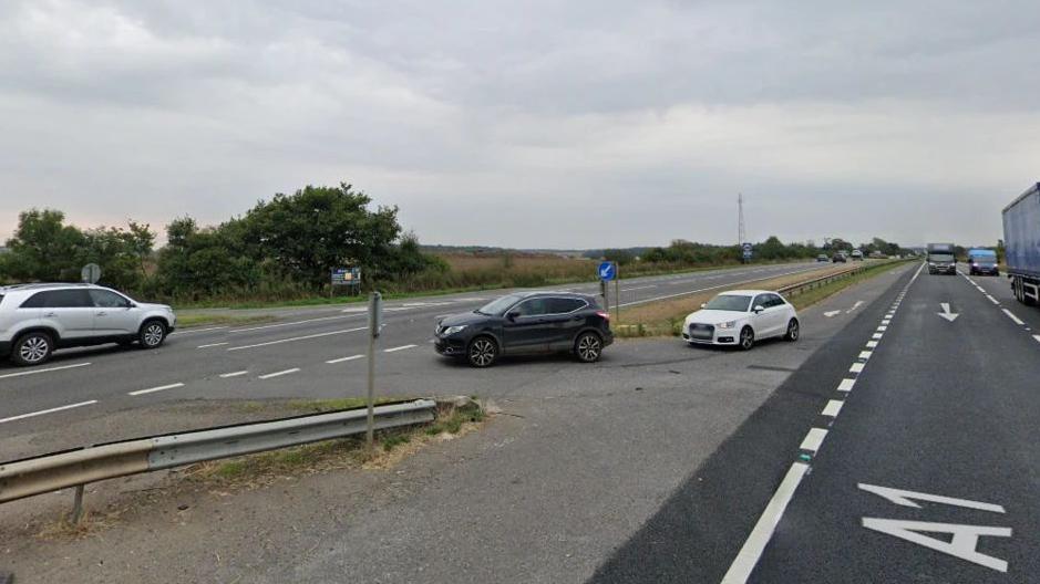 Two cars queue on a crossover point on the A1, where the is a gap in the central reservation. Either side of the central reservation there is a dual carriageway. 