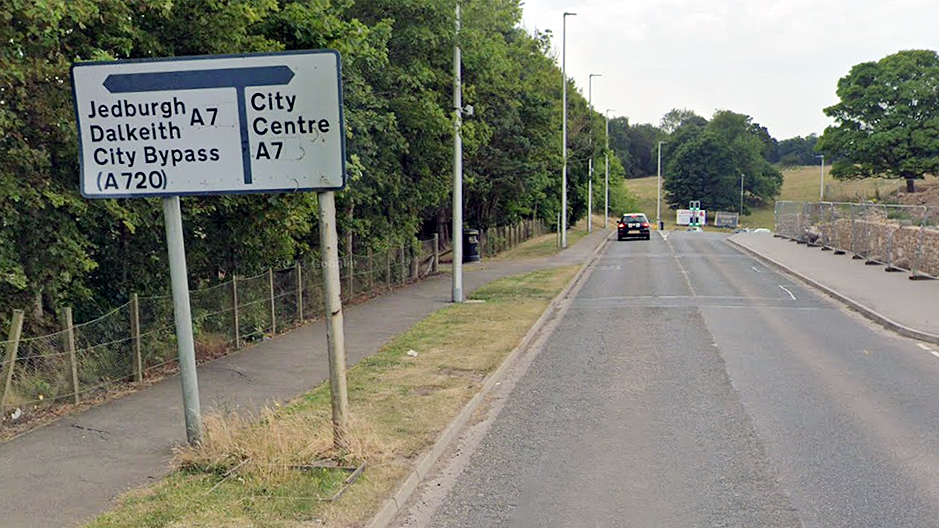 Roas sign to the left of road with a small car in distance