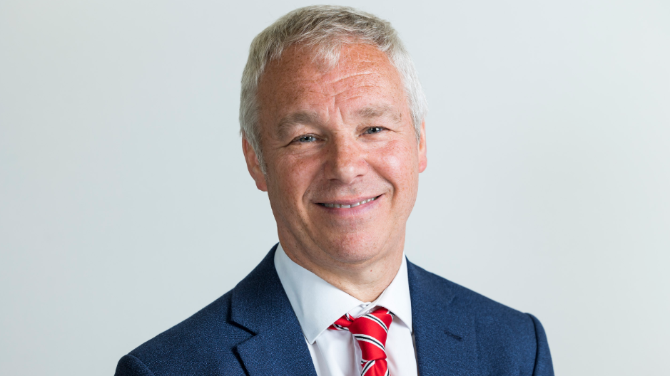 Councillor John Ennis smiles at the camera in his official council photo. He has light grey hair and wears a blue jacket, white shirt and red tie.