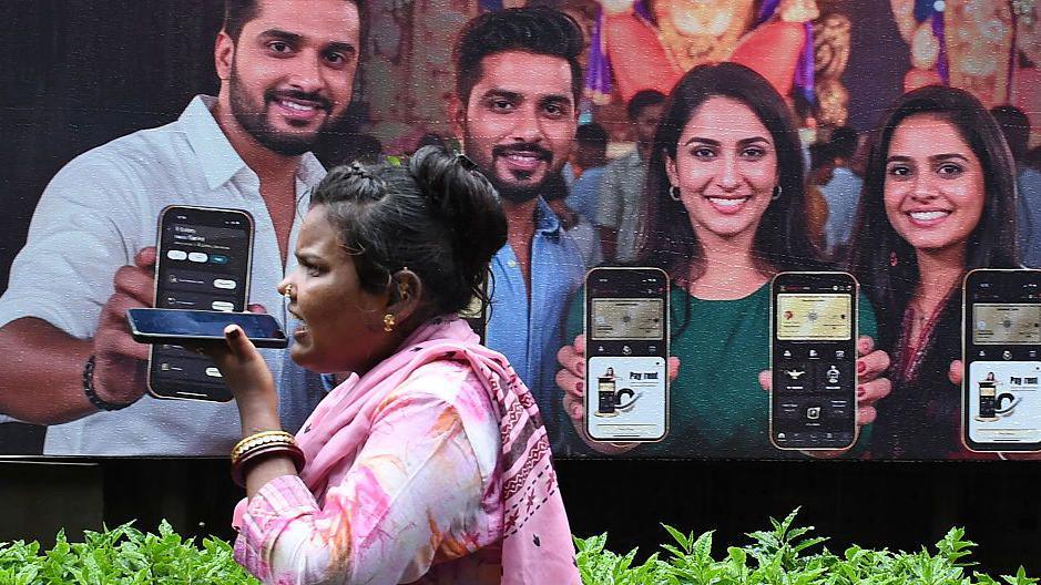 A woman wearing a pink Indian dress speaks on phone near a poster of a mobile phone advertisement in Mumbai city, with four models showcasing their smartphones. 