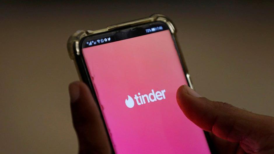 A close shot of a hand holding a smartphone with the pink background and logo of tinder dating app