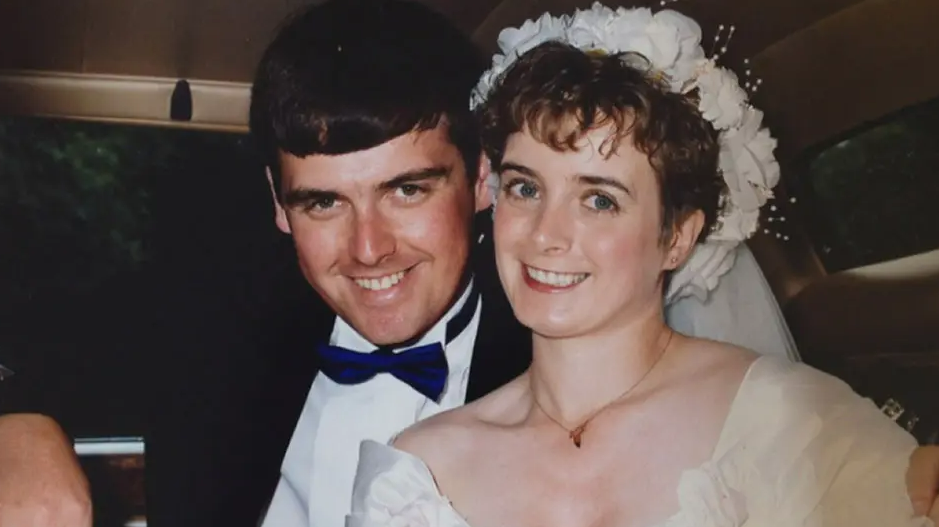 PC Lewis Fulton and wife Christine on their wedding day. PC Fulton is wearing a dark suit with a white shirt and blue bow tie. Christine is wearing a white dress and white floral headband with a veil at the back.