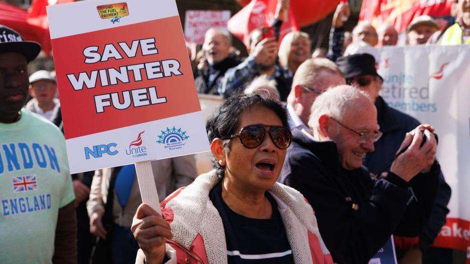 A woman holding a placard reading: "Save winter fuel", at a protest in central London in October 2024