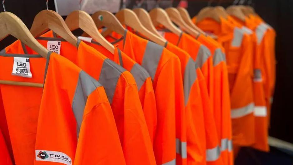 A row of hi-vis orange jackets on wooden coat hangers.
