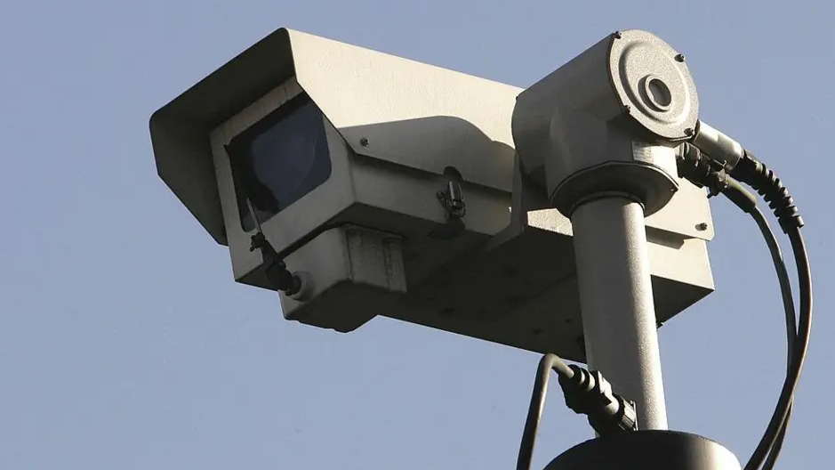 A close up of a grey CCTV camera with blue sky in the background