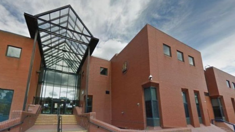 A large red-brick court building with steps up to a glass-fronted entrance below a glass canopy