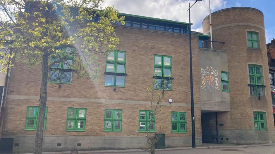 Luton Crown Court: a brown-brick building with green-framed windows. A tree with yellow leaves stands in front of the left side of the building.