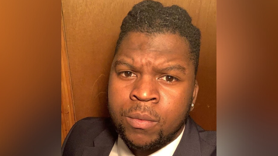 A selfie of a man with dark hair and a short dark beard, wearing a black and white suit.