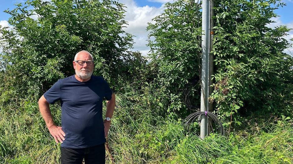 Jim Crawford standing outside next to a phone mast. A wire is next to it rolled up. He has his hands on his hips.