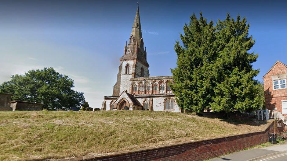 A large grey church sits behind a grass lawn with headstones.