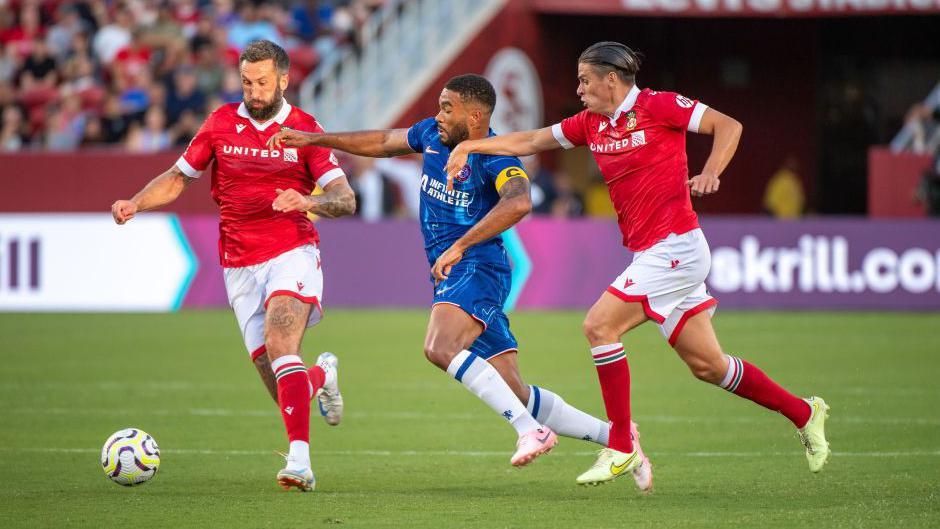 Ollie Palmer and George Dobson chase the ball for Wrexham either side of Chelsea's Reece James