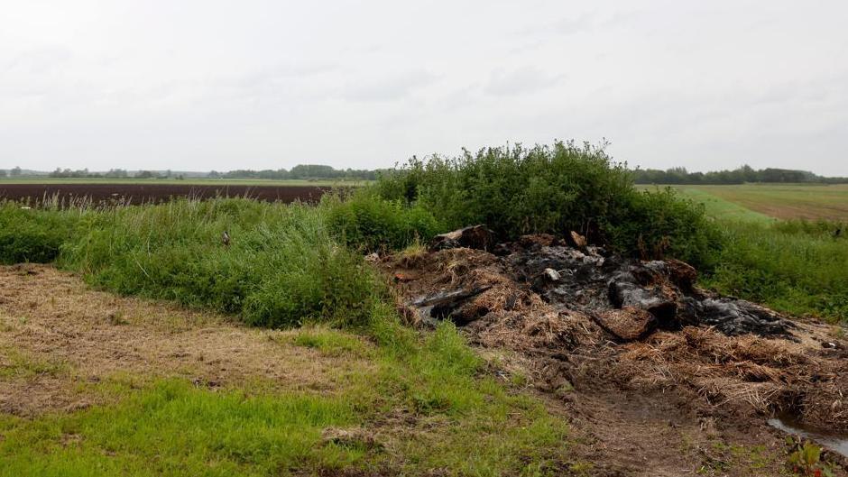 A bare farmer's field in Lincoln, damaged after flooding earlier in the year. Mud and debris is piled to the right-hand side, topped by green shrubbery.