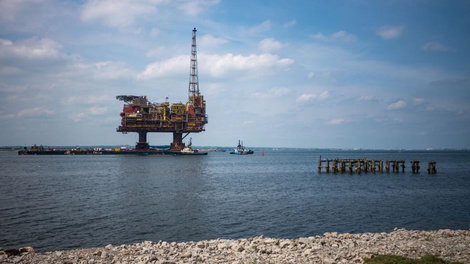 An oil rig in the North Sea pictured from a pebbly beach