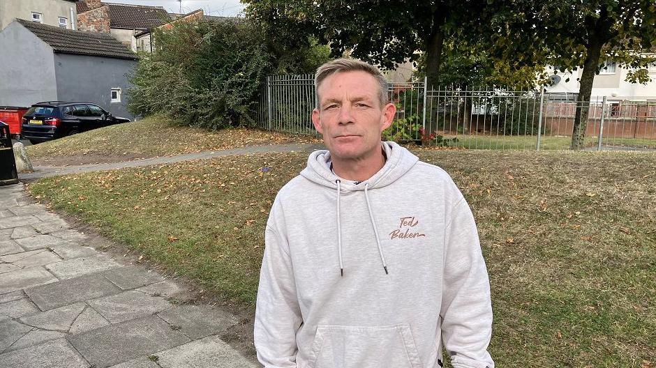 Jeff Rochford, who has light, short hair. He's wearing a grey hoodie and is standing in front of a patch of grass.