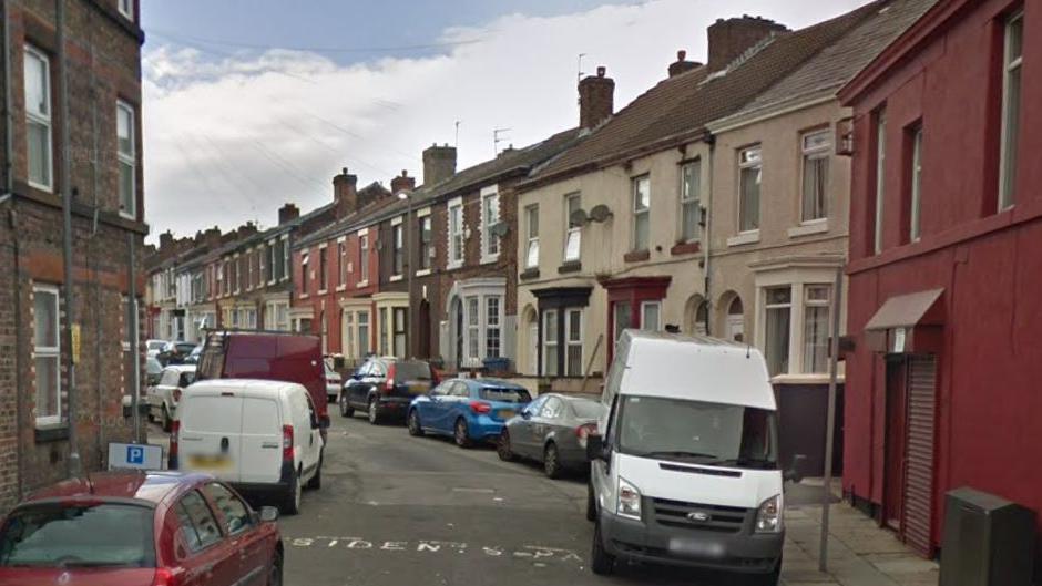 Street of terraced houses with cars and vans parked on road