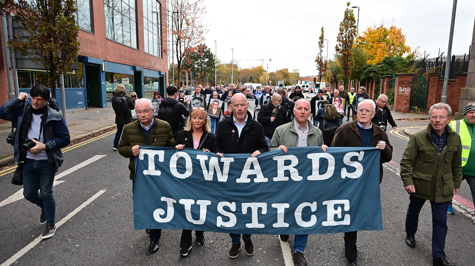Shows four men and a woman, second left, carrying a banner saying "Towards Justice"
