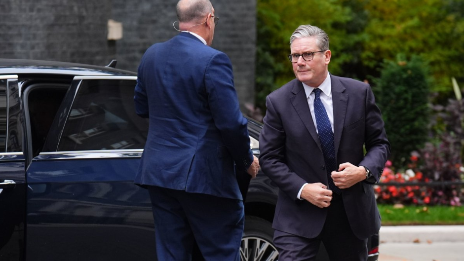 Keir Starmer walks out of his Prime Ministerial car outside No 10 Downing Street. He in correcting his suit blazer whilst his assistant closes the door behind him