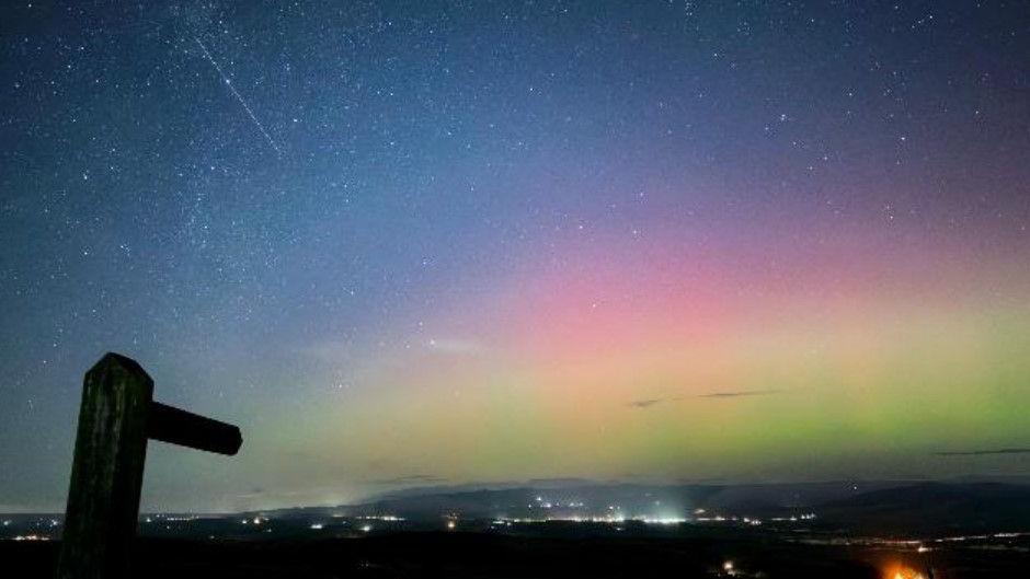 A starry sky glowing blue, pink and green with a signpost in the foreground.