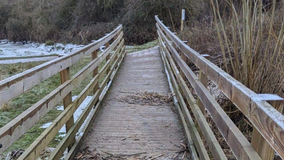 A wooden footbridge with wood panel railing either side.