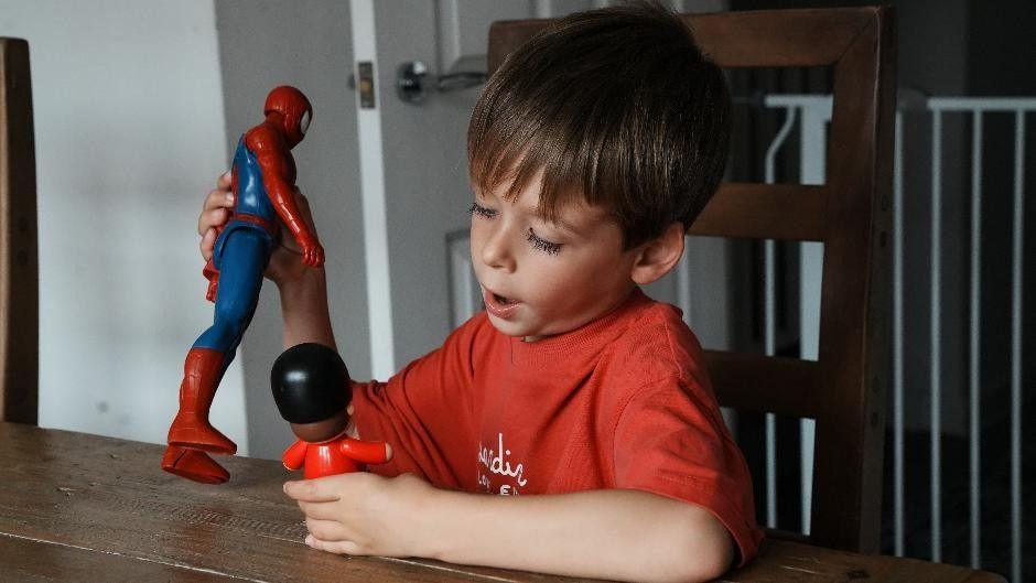 Freddie focused on playing with toys at the table, one is a Spider-Man figure