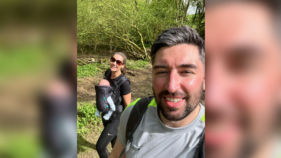 Tyler and Gabrielle on a walk in the sun with baby Bertie, who is strapped to Gabrielle's front in a baby carrier