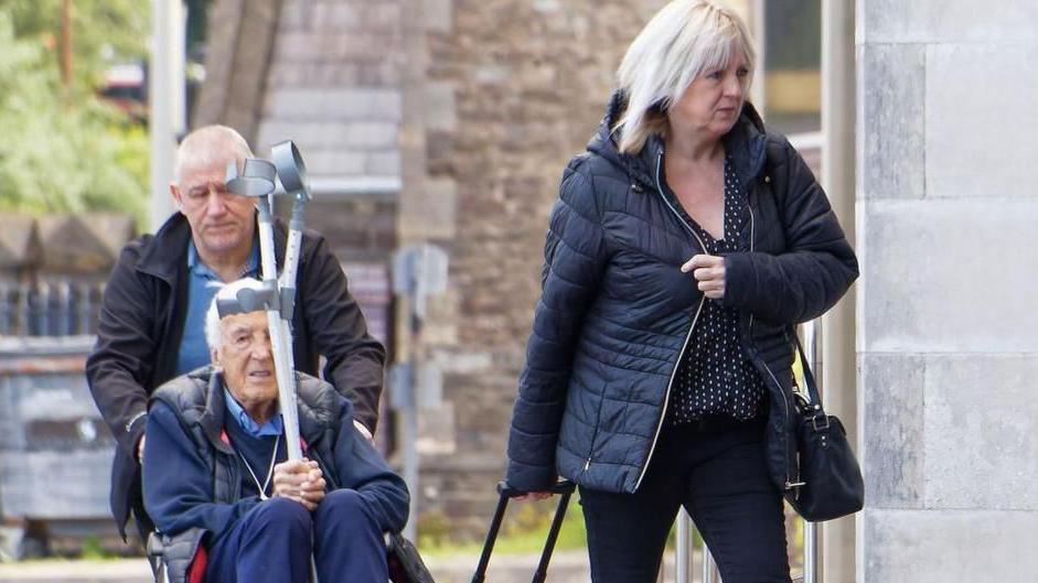 Gerald and Katherine Hill arriving at court. Gerard is in a wheelchair and is holding crutches
