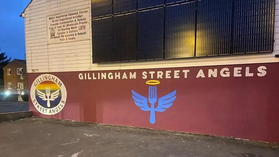 Gillingham Street Angels' site on Skinner Street. It is a white and red painted building with the charity's logo of a fork with wings spray painted onto its wall.