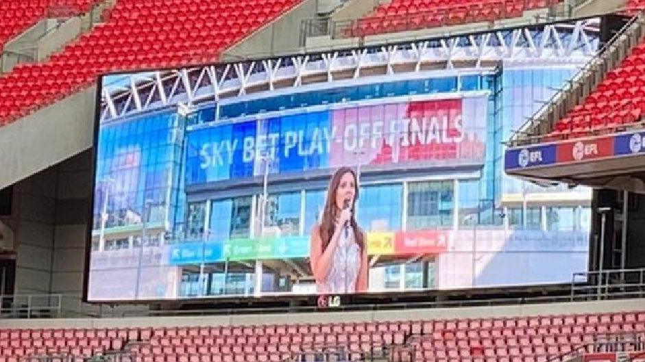 Empty football stadium with big screen showing Faryl Smith singing